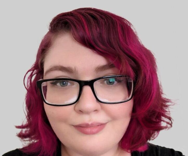 A person with red hair wearing black rim glasses